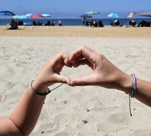 Two hands making a heart with their fingers on the beach.