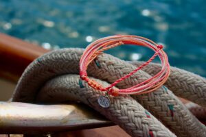 Red string bracelet with a silver charm on coiled rope by water.